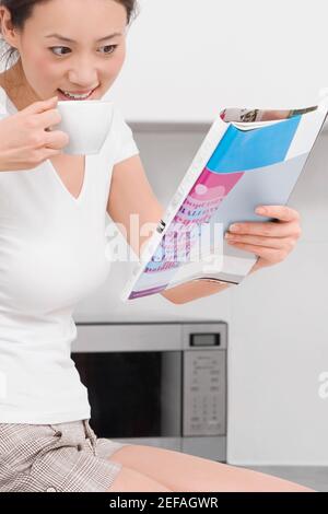 Seitenprofil einer jungen Frau, die Tee trinkt und liest Eine Zeitschrift Stockfoto