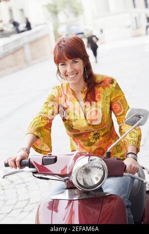 Porträt einer jungen Frau, die auf einem Motorroller sitzt Und lächelnd Stockfoto