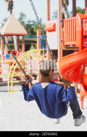 Rückansicht eines Jungen im Teenageralter, der an einer Kette schwingt Swing-Fahrt Stockfoto