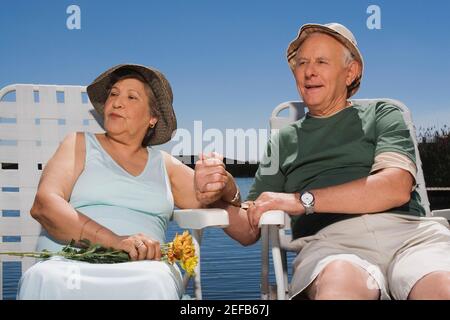 Ältere Paare sitzen am See mit Händen halten Einander Stockfoto