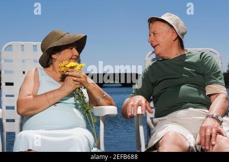 Ein Seniorenpaar sitzt am See und schaut sich jedes an Andere Stockfoto