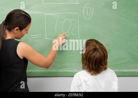 Rückansicht einer Lehrerin, die einen Schuljungen unterrichtet Ein Klassenzimmer Stockfoto