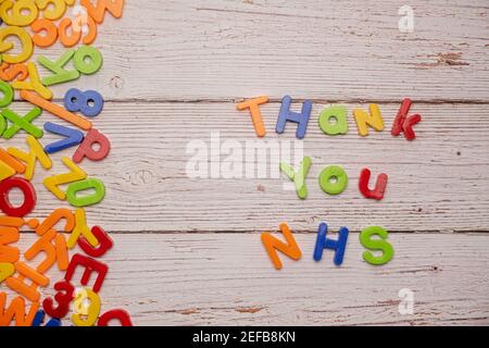 Bunte Magnetbriefe auf einem rustikalen weißen Tisch zu Hause Schule Coronavirus Rechtschreibung Danke NHS Stockfoto