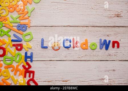 Bunte Magnetbriefe auf einem rustikalen weißen Tisch zu Hause Schule Coronavirus Rechtschreibung LOCKDOWN mit einem Buchstaben trägt ein Gesichtsmaske Stockfoto