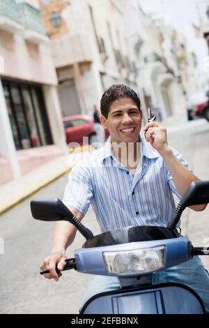 Porträt eines jungen Mannes auf einem Motorroller und Sprechen auf einem Mobiltelefon Stockfoto