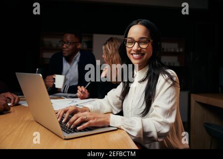 Porträt einer jungen erfolgreichen Geschäftsfrau, die während der Kamera schaut Besprechen Sie mit ihrem Team mithilfe eines Laptops das Projekt im Hintergrund Stockfoto