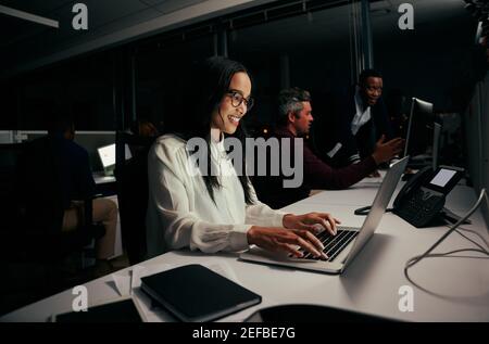 Weibliche Angestellte beschäftigt in ihrer Arbeit auf Laptop im Büro Und mit Kollegen im Hintergrund Stockfoto