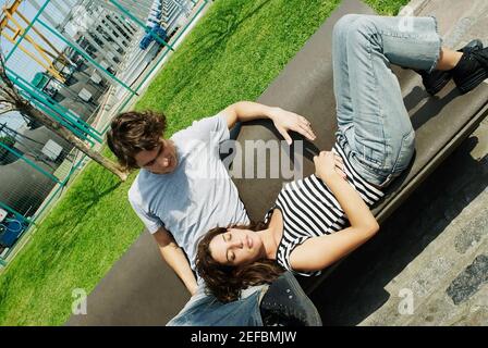 Junge Frau, die auf einer Bank liegt und ihren Kopf darin ruht Der Schoß eines jungen Mannes Stockfoto