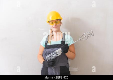 Die Frau macht selbständig Reparaturen im neuen Haus, hält den Mixer für das Mischen des Putzes an den Wänden. Stockfoto