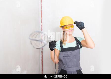 Die Frau macht selbständig Reparaturen im neuen Haus, hält den Mixer für das Mischen des Putzes an den Wänden. Stockfoto