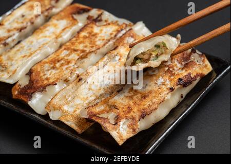 Material der traditionellen chinesischen frittierten Knödel (auch genannt Gyoza, Topf Aufkleber) auf schwarzem Hintergrund mit Essstäbchen. Stockfoto