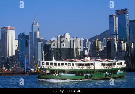 Fähre im Meer vor Wolkenkratzern, Hongkong, China Stockfoto