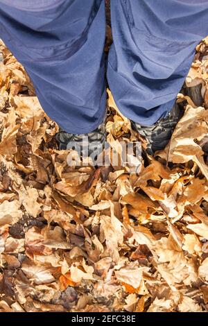 Füße in blauer Jogginghose und schwarzen Sneakers stehen im Herbstlaub. Vertikale Ausrichtung Stockfoto