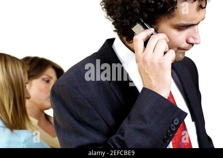 Geschäftsmann, der mit seinen beiden Sekretärinnen auf einem Mobiltelefon spricht Hinter ihm stehen Stockfoto