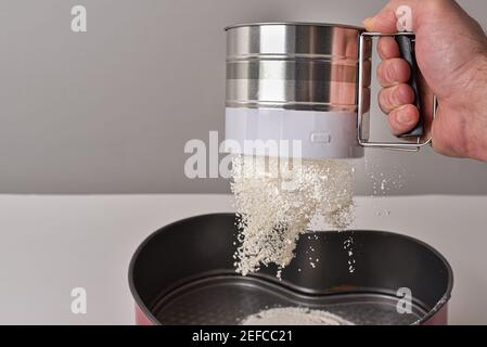 Sieben Sie die männliche Hand eines Konditors. Sieben und Belüften von Mehl zum Backen. Stockfoto