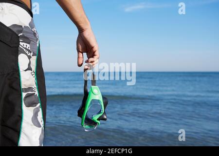 Mittlere Ansicht eines Mannes, der eine Schwimmbrille hält Stockfoto