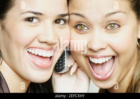 Portrait von zwei jungen Frauen, die ein Handy hören Und lächelnd Stockfoto