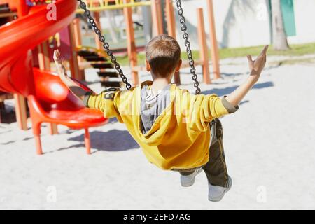 Rückansicht eines Jungen, der auf einer Kettenschwinge schwingt Fahrt mit ausgestrecktem Arm Stockfoto