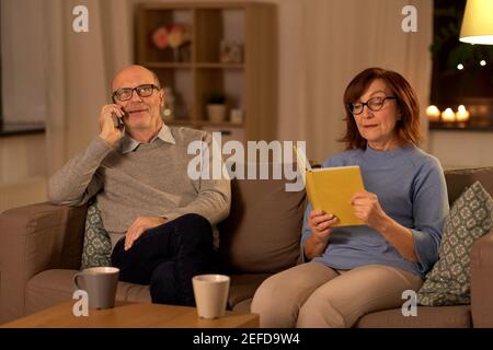 Seniorenpaar mit Buch und Smartphone zu Hause Stockfoto