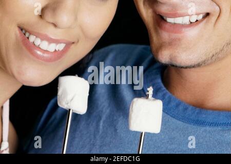 Nahaufnahme eines jungen Paares mit zwei Marshmallows auf Spiessen Stockfoto