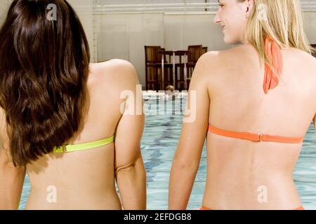 Rückansicht von zwei jungen Frauen, die am Rand sitzen Eines Schwimmbades Stockfoto