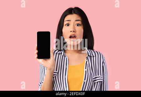 Neue App Porträt schockiert erstaunt junge asiatische Frau hält Smartphone mit schwarzem leeren Bildschirm in der Hand, zeigen Gerät. Gadget mit leerem freien Speicherplatz Stockfoto