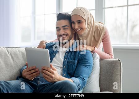 Attraktive muslimische Paar bärtige Kerl und junge Dame in Hijab mit Videokonferenz über digitale Tablette während zu Hause bleiben während covid-19 Pandemie, m Stockfoto