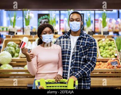 Porträt eines schwarzen Paares, das während einer Coronavirus-Pandemie Schutzmasken trägt und eine Kreditkarte im Einkaufszentrum hält. Millennial African American gu Stockfoto