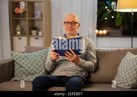 Glücklicher kahler älterer Mann auf dem Sofa, der zu Hause Buch liest Stockfoto