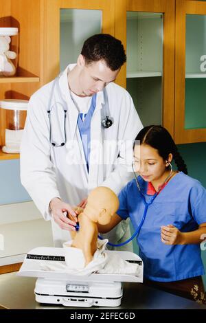 Mädchen untersucht eine Puppe mit einem Stethoskop und einem Männchen Doktor, der neben ihr steht Stockfoto