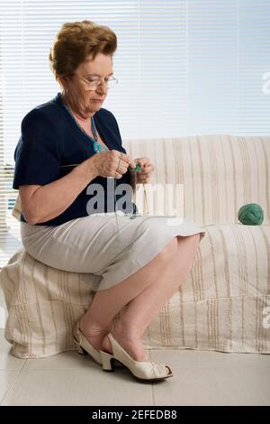 Ältere Frau sitzt auf einer Couch und strickt Stockfoto