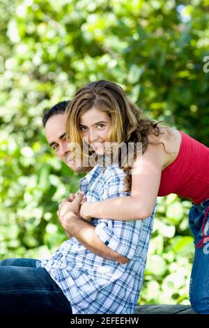 Porträt einer jungen Frau, die einen Mitte erwachsenen Mann von hinten umarmen Stockfoto