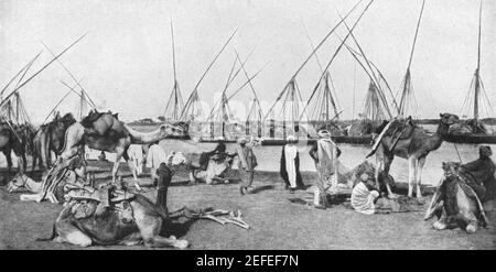 Anfang 20th Jahrhundert Foto des Hafens von Omdurman mit Sudanesische Händler und eine Kamelkarawane am Ufer Der Weiße Nil mit Handelsbooten oder Felucken im Hintergrund ca. Anfang 1900s Stockfoto