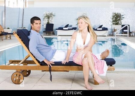 Porträt einer jungen Frau und eines mittleren erwachsenen Mannes Sitzen auf einem Liegestuhl am Pool Stockfoto