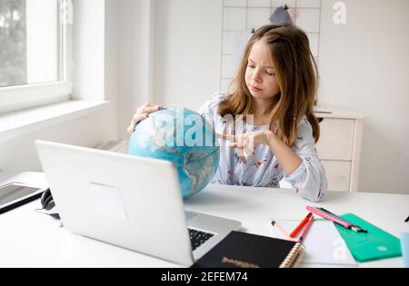 Schönes, junges, blondes Mädchen sitzt vor dem Laptop und hält den Globus in den Händen und träumt von Urlaub und Ende der Pandemie Stockfoto