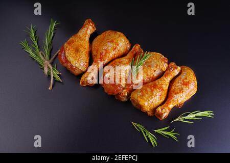 Frische Hähnchenschenkel. Roher Hähnchendrumstick mit Gewürzen und grünem Rosmarin auf schwarzem Hintergrund. Rohe Hähnchenspieße auf Spieße.Convenience Food, preco Stockfoto