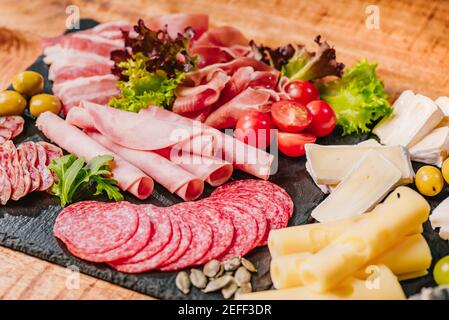 Die Wurstwaren verschiedener Art auf schwarz Flacher Teller auf einem Holztisch mit Gemüse.verschiedene Arten von Wurst mit Käse auf Woo serviert Stockfoto