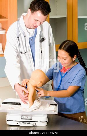 Mädchen untersucht eine Puppe mit einem Stethoskop und einem Männchen Doktor, der neben ihr steht Stockfoto