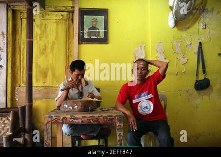 Handwerker macht eine Lederpuppe für wayang kulis Theater im klassischen Wayang Handwerksladen in Yogyakarta, Zentral Java, Indonesien. Rechts ist der Bastelmanager Dodo mit einem blauen Hemd abgebildet. Auf der gelben Wand ist das Porträt des Gründers des Kunsthandwerksladens zu sehen. Kanjeng Raden Tumenggung Djojojodiningrat, der Urgroßvater des heutigen Besitzers des Kunsthandwerks, war der Hofpuppenmeister des Sultans Hamengkubuwono IX. Von Yogyakarta. Das liegt daran, dass das Classic Wayang direkt im Yogyakarta Keraton, dem Bereich des Sultanspalastes, liegt. Traditionelle Puppe Schatten thea Stockfoto