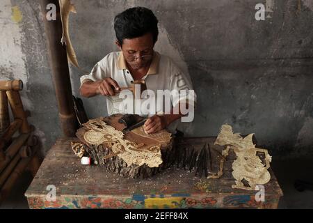 Handwerker macht eine Lederpuppe für wayang kulis Theater im klassischen Wayang Handwerksladen in Yogyakarta, Zentral Java, Indonesien. Das traditionelle Puppenschattentheater Wayang kulit ist auf den Inseln Java und Bali in Indonesien weit verbreitet. Puppen für Wayang kulis sind aus Büffelleder gefertigt. Die Herstellung einer Puppe dauert etwa sechs Tage. Jeder Charakter hat seine eigenen Eigenschaften und kann leicht von den Zuschauern identifiziert werden. Stockfoto