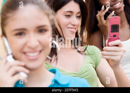 Teenager Mädchen Blick auf ein Handy mit zwei anderen Teenager-Mädchen sprechen auf Handys Stockfoto