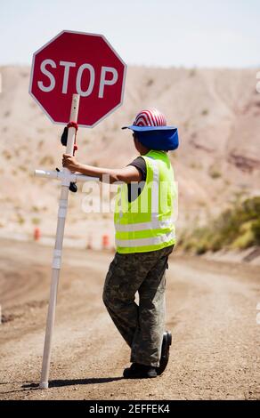 Seitenprofil eines Mannes, der ein Stoppschild hält Eine unbefestigte Straße Stockfoto