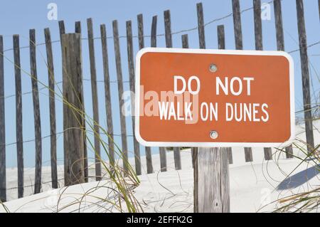 Braunes Schild mit der Aufschrift „Don't walk on Dunes“ mit einem Holzzaun und Sanddünen im Hintergrund Stockfoto