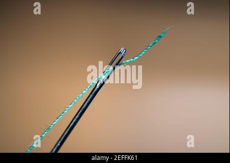 Nahaufnahme des Nadelauges mit blauem Faden, der durch das Nadelöhr geht, orangefarbener Hintergrund Stockfoto