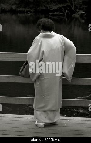 Alte Dame im Kimono, die Karpfen in Meiji Jingu innen füttert Garten im Winter Stockfoto