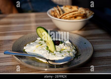 Echte authentische Foto von frischen griechischen Tzatziki Joghurt Dip und Pita Brot und Gurken im Restaurant unter goldener Sonneneinstrahlung Stockfoto