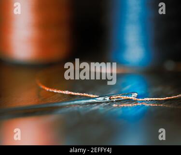 Nadel mit Gewinde auf Tisch mit Orange und Blau Spulen in Hintergrund Stockfoto