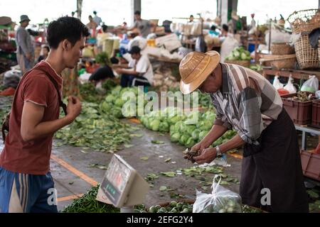 YANGON, MYANMAR - DEZEMBER 31 2019: Zwei burmesische Männer tauschen Geld aus, wenn sie Gemüse und Obst auf einem Straßenmarkt kaufen und verkaufen Stockfoto