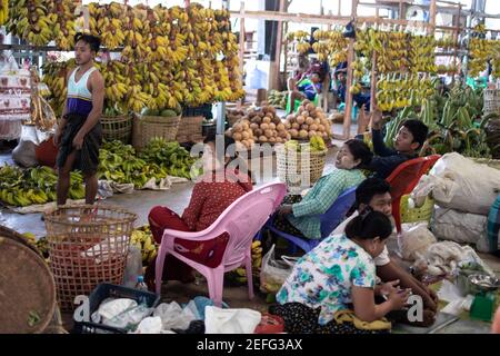 YANGON, MYANMAR - DECEMEBER 31 2019: Burmesen besuchen einen Straßenmarkt mit vielen Bananen und Kokosnüssen Stockfoto