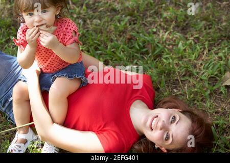 Porträt einer jungen Frau mit ihrer Tochter auf dem Bauch sitzen auf dem Rasen liegend Stockfoto